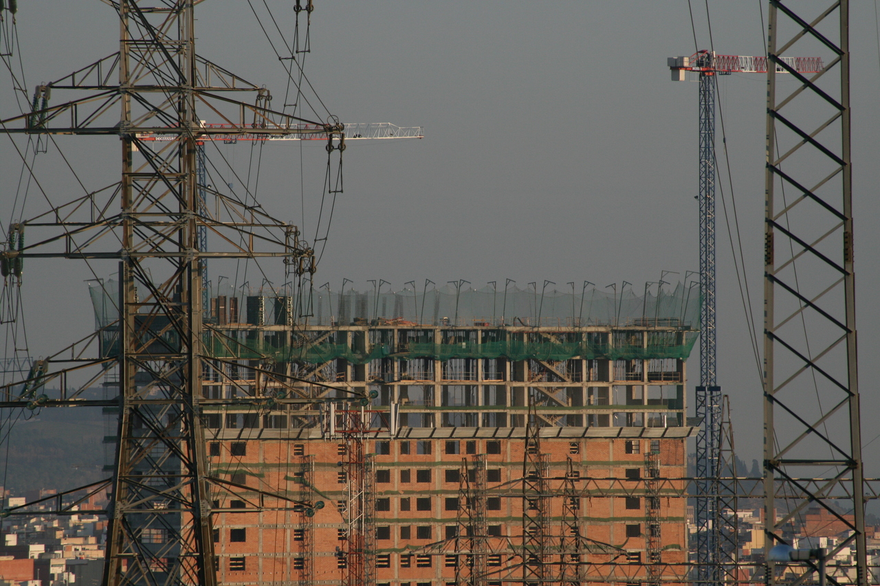Photo description: Gran edificio en obras al fondo. Torres de alta tensión con sus cables inundan la imagen.