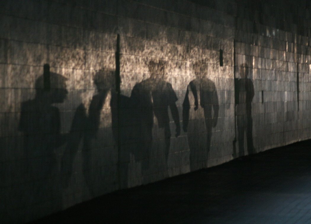 Photo description: Sombras de personas sobre una pared. Parece que están caminando y que dos de ellas conversan.