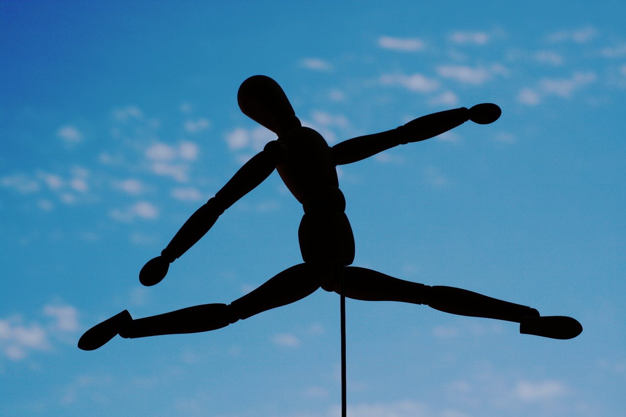 Muñeco articulado en posición de danza clásica, con el cielo azul de fondo.